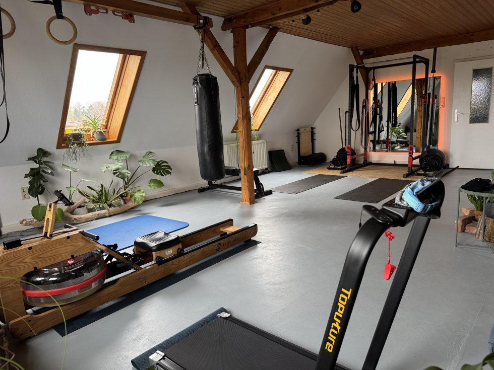 Trainingsraum im Wellness Atelier Hermle in Groß Molzahn: heller Dachraum mit Holzbalken, Dachfenstern, Boxsack und Trainingsgeräten