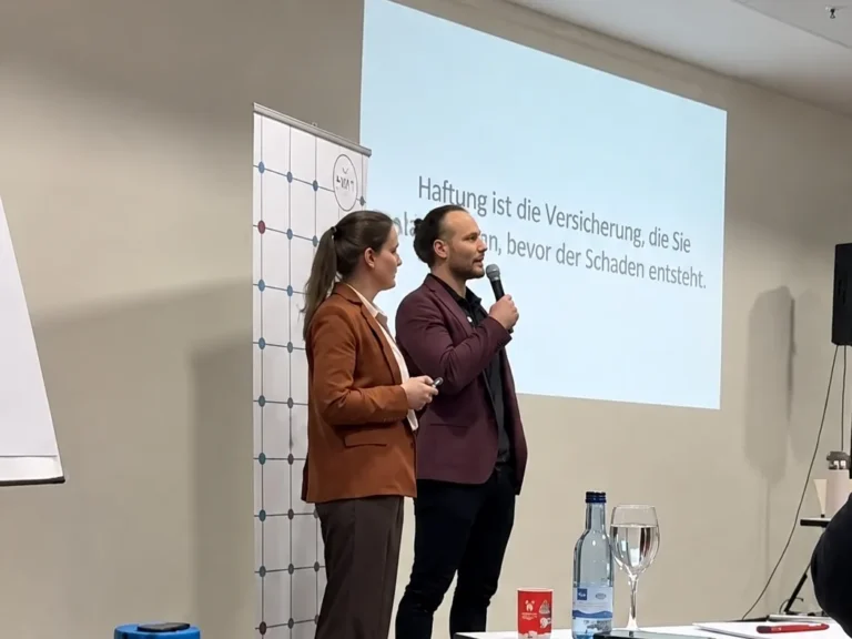 Tim Hermle spricht bei einem Vortrag ins Mikrofon, neben ihm steht eine Frau vor der Präsentationsleinwand