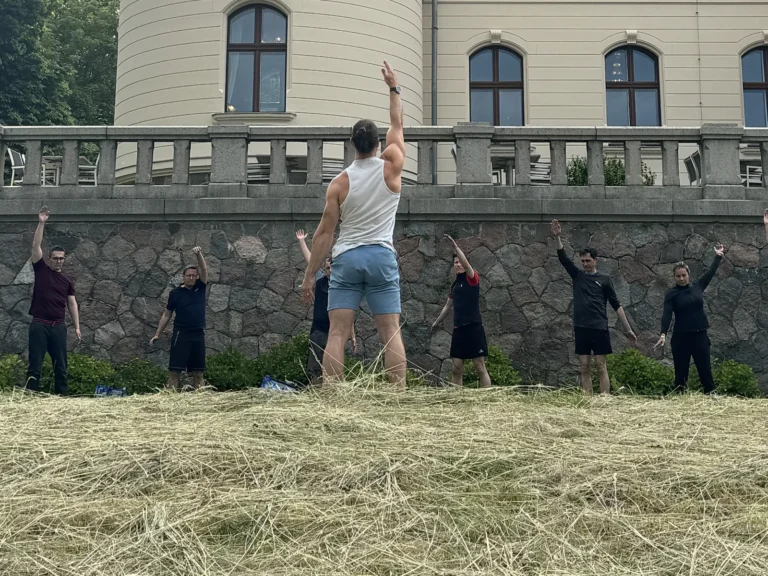 Trainer und Gruppe strecken sich im Stehen mit erhobenem Arm vor der Schlossmauer von Schloss Ralswiek