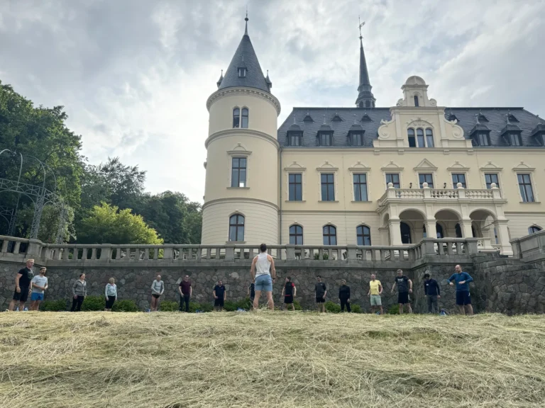 Eine Gruppe steht im Park vor dem Schloss Ralswiek und folgt den Anweisungen des Trainers bei einer Bewegungsübung