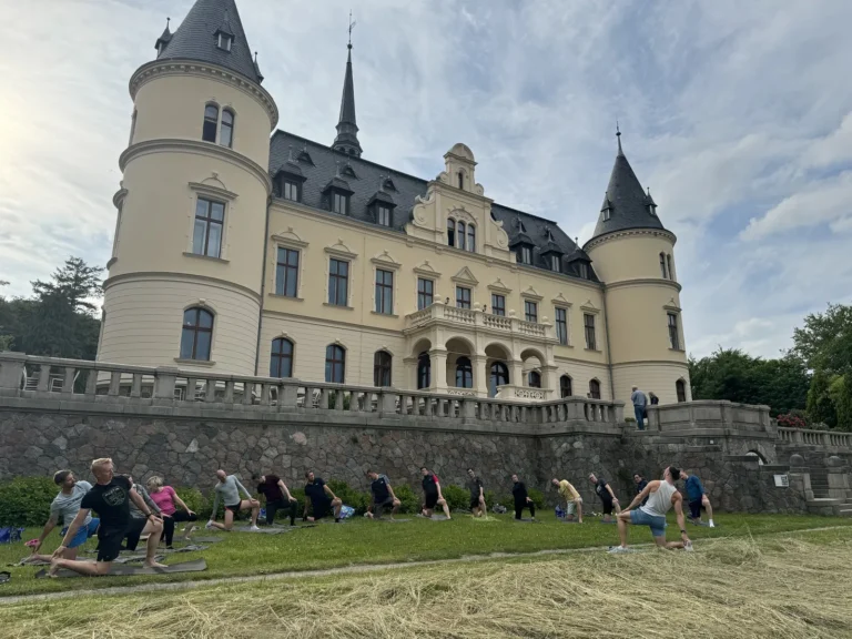 Teilnehmende einer Firmen-Yogastunde im tiefen Ausfallschritt auf Matten im Park vor dem Schloss Ralswiek auf Rügen