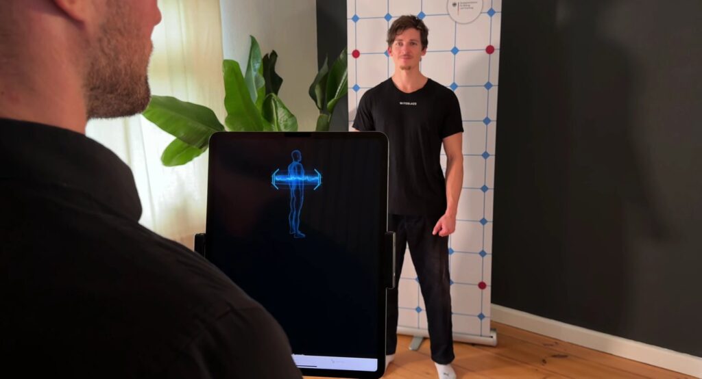 KI-Haltungsanalyse im Wellness Atelier Hermle: Das Tablet zeigt die Körpervermessung, der Kunde steht vor dem Messraster